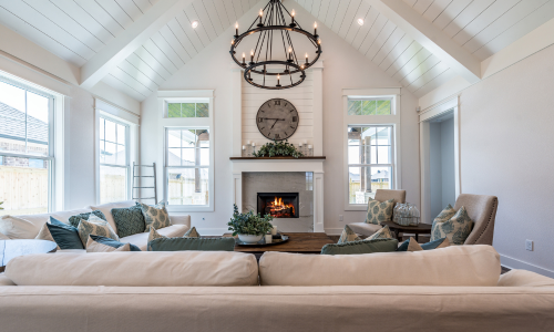 "Living room with a fireplace, chandelier, two couches, chairs, four windows, and a shiplap ceiling with beams.